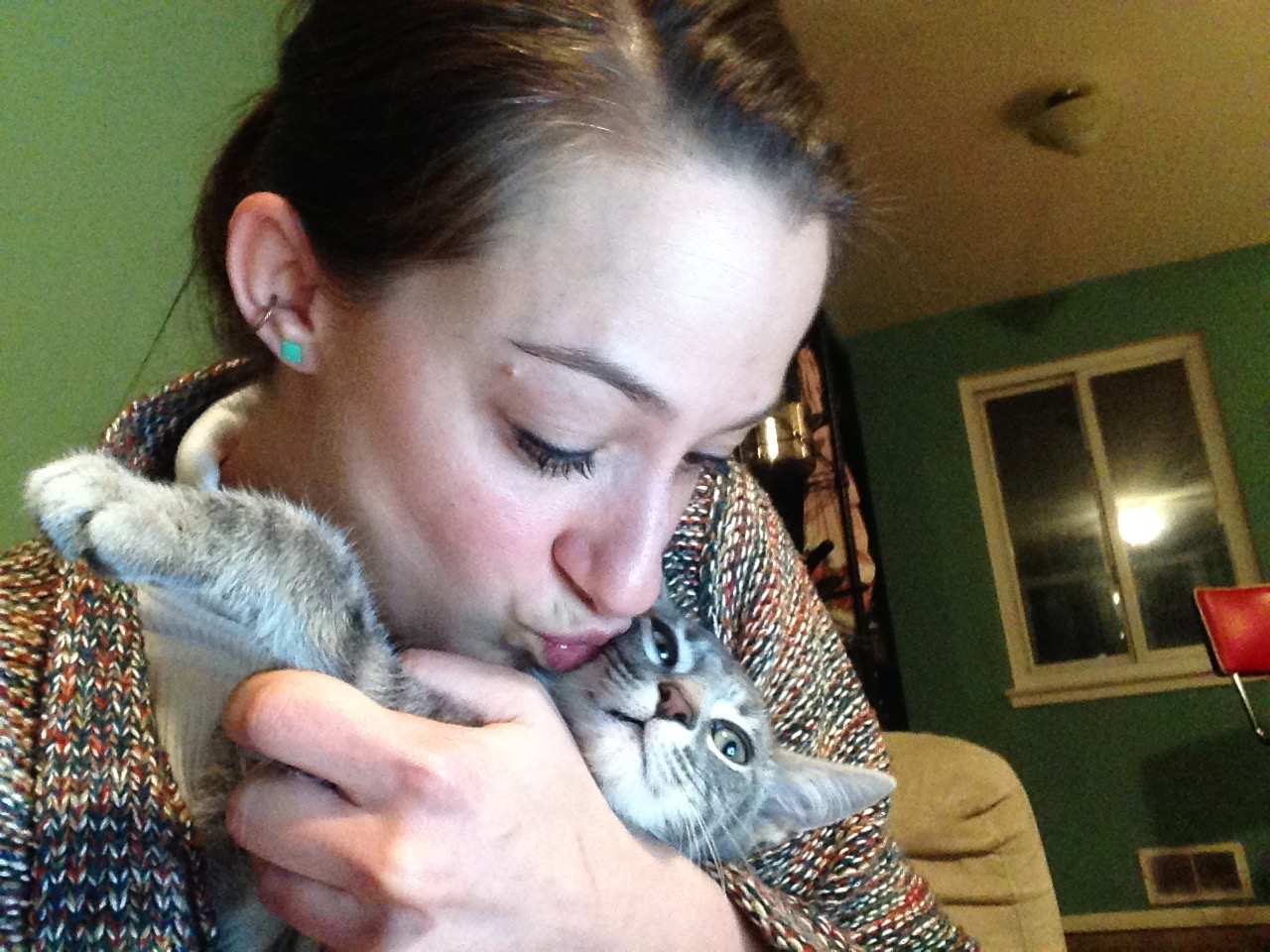 Photo of Amber Freiwald, indoors, hugging and kissing a gray and white cat
